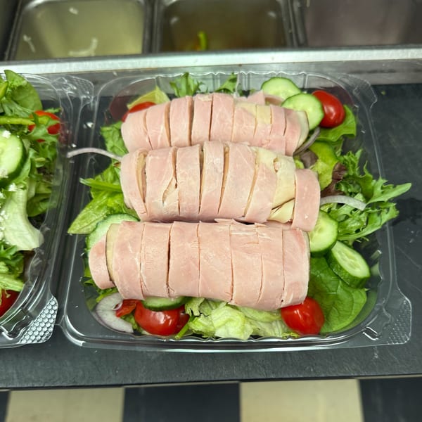 Two plastic containers of salads with ham and cheese rolls, lettuce, cucumbers, and cherry tomatoes.